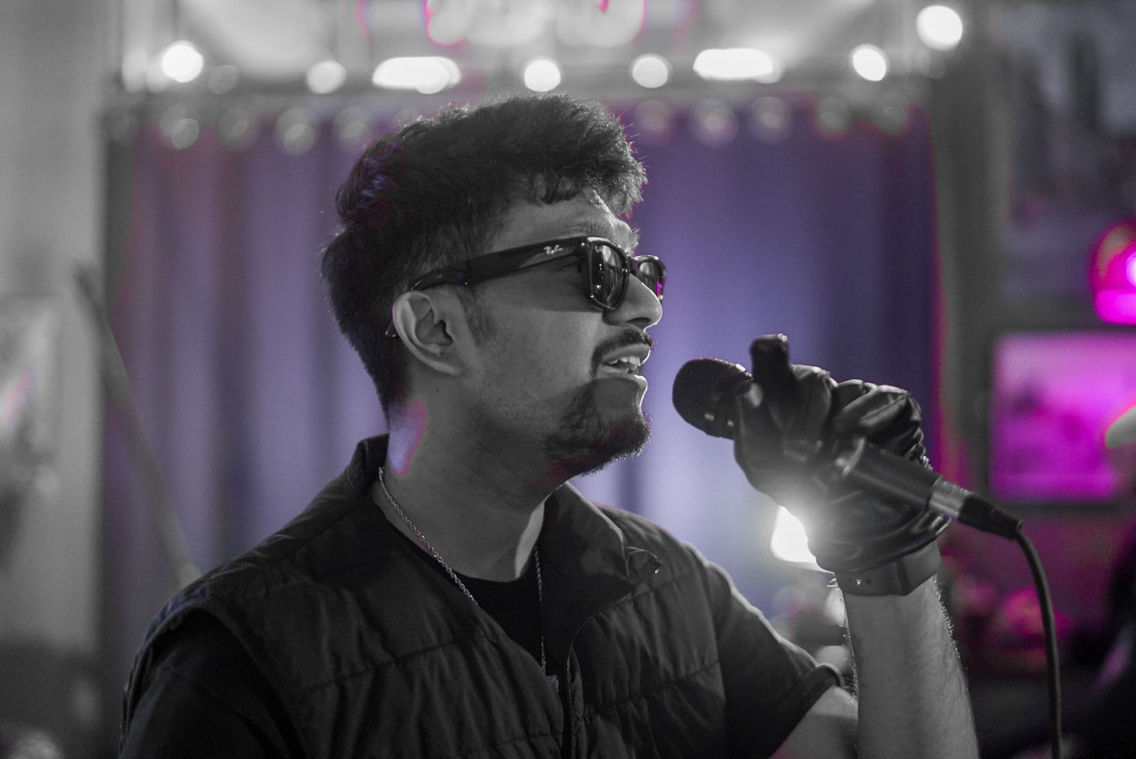 SUSH 28 singing into a microphone in sunglasses, in black and white with purple stage light