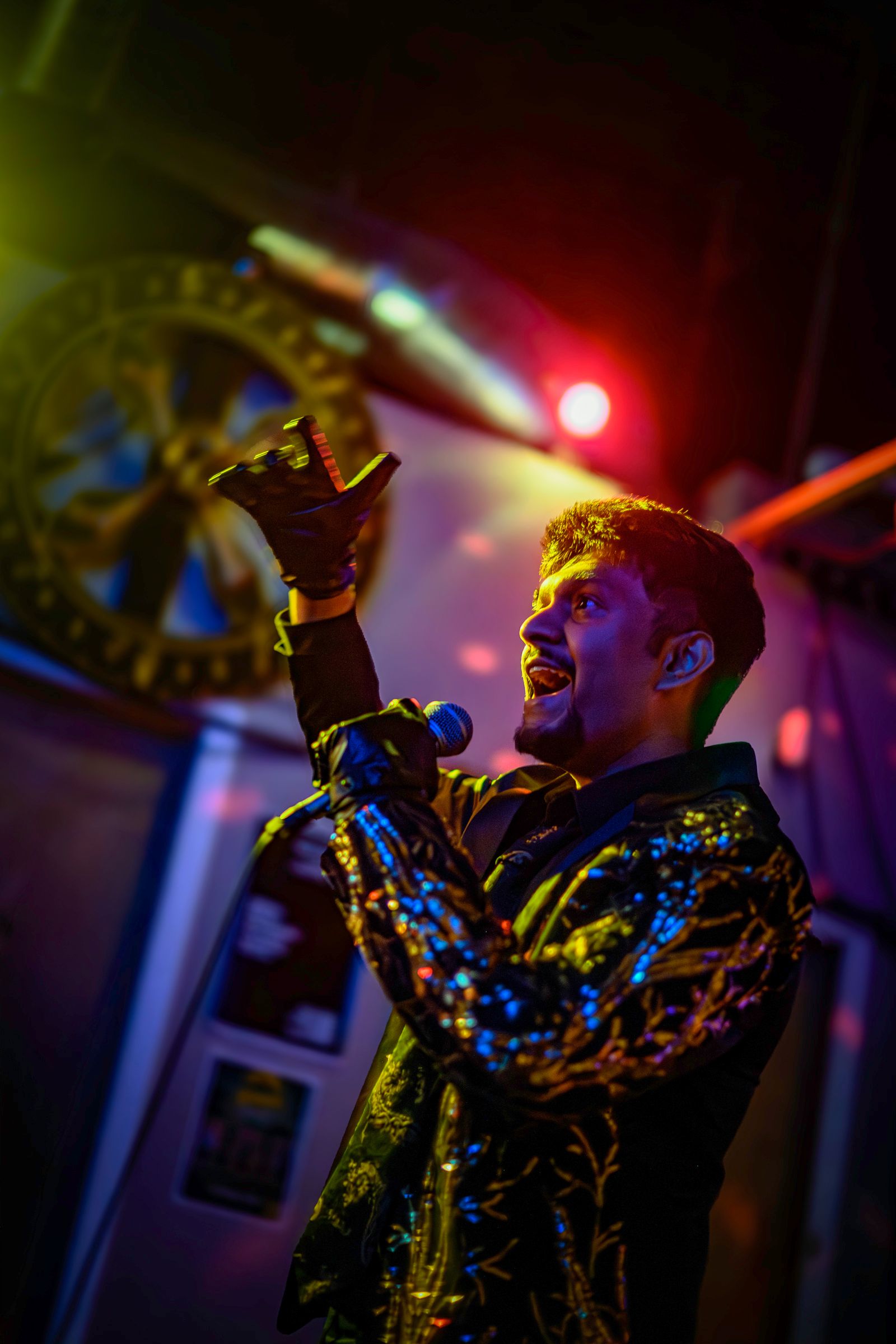 SUSH 28 on stage reaching up with a gloved hand while singing, lit in blue and orange